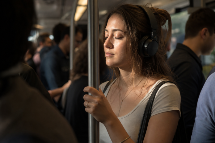 Young woman with headphones on a crowded morning train Young woman with headphones and eyes closed on a crowded commuter train in morning light, other passengers blurred