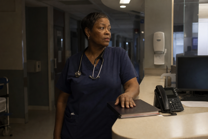 How to Open Up Your Intuition: a nurse pausing on a night shift Experienced nurse in scrubs pausing at a hospital ward station at night with a hand on a chart, listening down the corridor