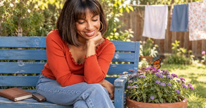 The Spiritual Meaning of Butterflies: Change, Memory and Personal Meaning Woman quietly watching a butterfly on a flower in a modest garden