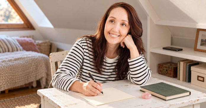Woman writing a thoughtful letter beside a simple reflection journal at home