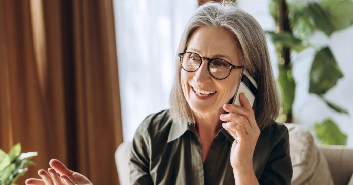 A woman with glasses talking on a phone in her living room.