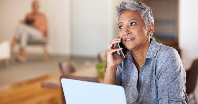 A woman having a phone conversation beside a laptop at home.
