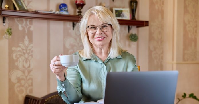 Woman with a warm drink beside her laptop at home