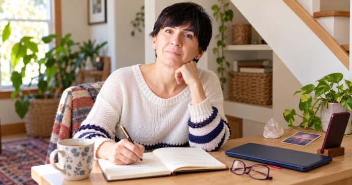 Woman writing an honest reflection beside a closed laptop